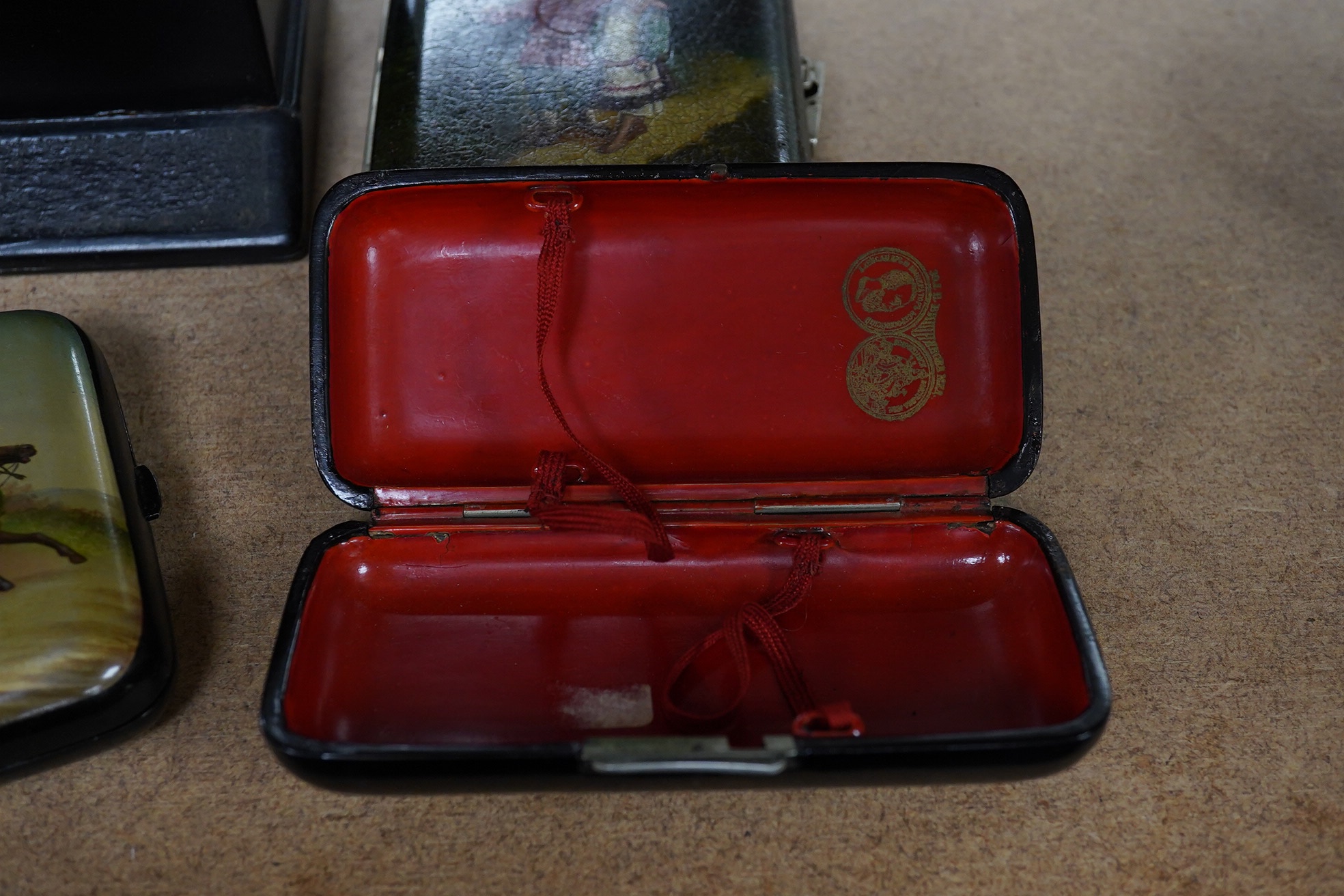 Three Russian lacquer cigarette cases, late 19th/early 20th century, one decorated with a troika scene and a match strike, 11cm wide. Condition - good